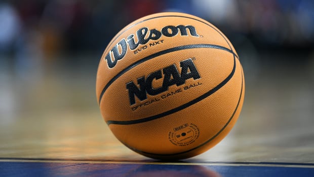 An NCAA basketball rests on a hardwood floor.
